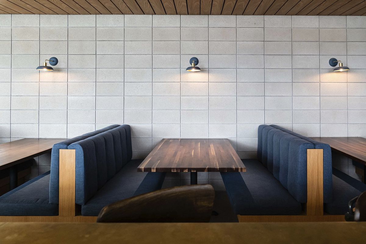  Back-to back blue,upholstered booth seating against a tiled wall with a wood slatted ceiling.
