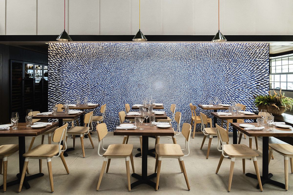  A restaurant dining room, in which rows of tables are set against a large piece of artwork.
